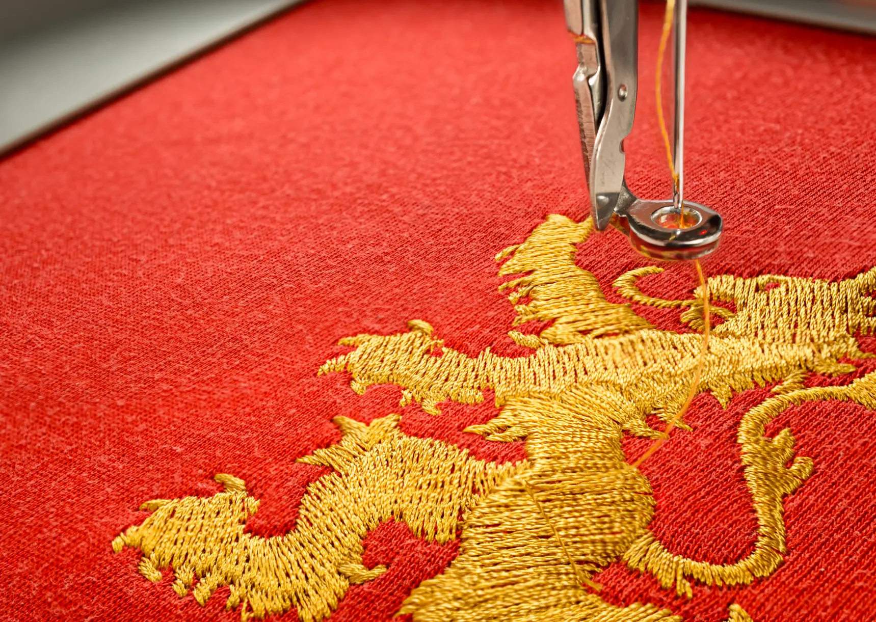 A sewing machine is embroidering a gold lion design on red fabric.